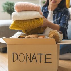 A woman stacking clothing into a donation box labelled 